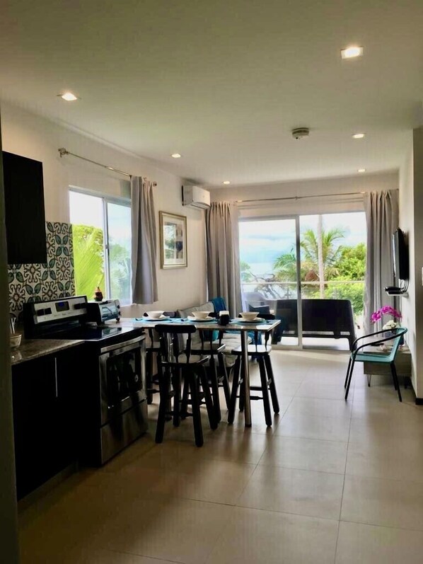 A modern kitchen with a dining area, large windows, and a view of the outdoors.
