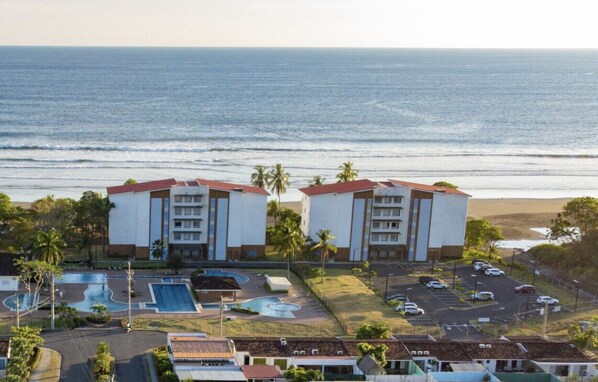 A beachfront hotel with two buildings, a swimming pool, and a parking lot.