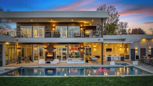 A modern two-story house with a swimming pool, outdoor seating, and a well-lit interior. - Lake Norman Lakefront - Pickleball, Hot Tub, Pool (Mooresville)
