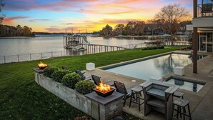 A swimming pool with a fire pit and outdoor seating, overlooking a body of water with a dock and boats. - Lake Norman Lakefront - Pickleball, Hot Tub, Pool (Mooresville)