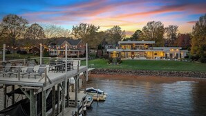 A lakeside property with a dock, a large house with a deck, and a boat. - Lake Norman Lakefront - Pickleball, Hot Tub, Pool (Mooresville)