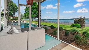 A modern living room with a large window overlooking a pool and a lake. - Lake Norman Lakefront - Pickleball, Hot Tub, Pool (Mooresville)