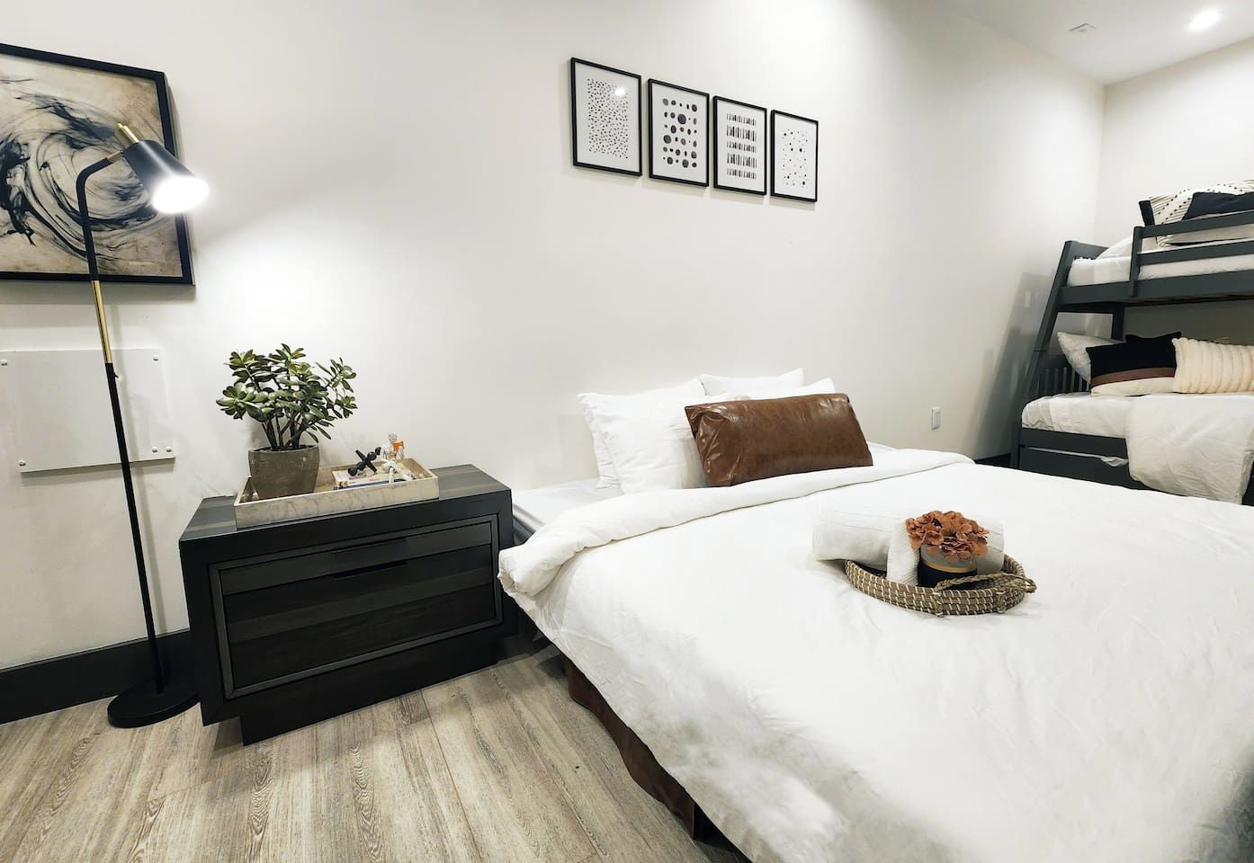 Una habitación de hotel moderna con cama, mesita de noche, lámpara, obra de arte y literas.