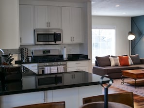 A modern kitchen with white cabinets, a stainless steel stove, and a microwave. There is a dining area with a wooden table and chairs.