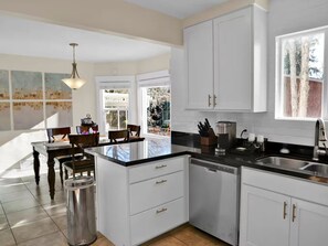 Enjoy meals in this kitchen with a dishwasher, sink, and dining area with a table and chairs, offering a view of the surrounding trees.