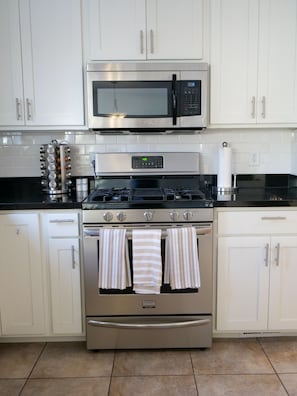 Fully equipped kitchen with stainless steel appliances, white cabinets, and a black countertop.