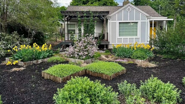 Uma casa com varanda, cercada por um jardim com diversas plantas e flores.