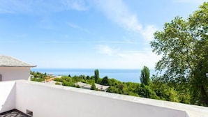 A balcony with a patterned floor, overlooking a coastal landscape with trees and a view of the sea. - Gems of Zagora (Zagora-Mouresi)