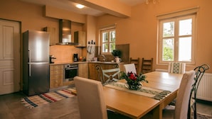 A modern kitchen with a refrigerator, stove, and dining area with chairs and a table. - Gems of Zagora (Zagora-Mouresi)