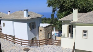 A white building with a stone facade, a wooden fence, and a view of the sea. - Gems of Zagora (Zagora-Mouresi)