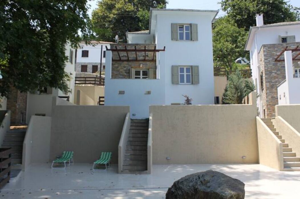 Un edificio residencial con una escalera que lleva al segundo piso, dos sillones de color verde con rayas y una gran roca al frente.