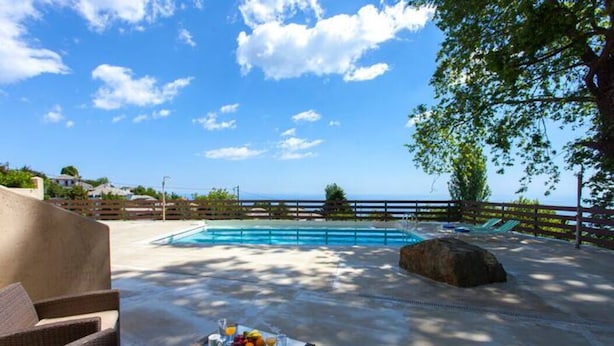 A poolside area with lounge chairs, a table with fruit and drinks, and a view of the sea. - Gems of Zagora (Zagora-Mouresi)