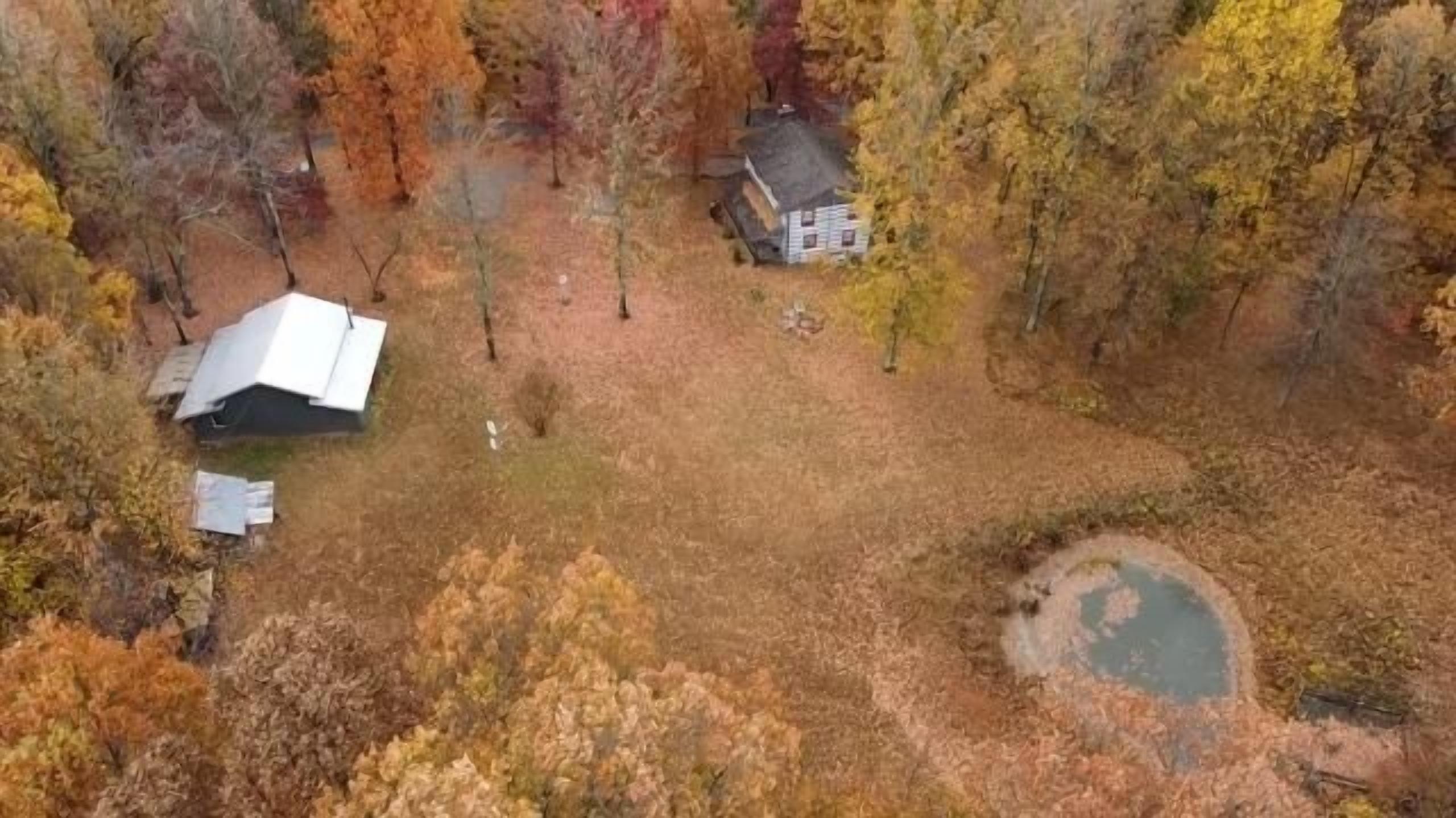Vista aérea de una propiedad con un patio amplio y abierto, un estanque pequeño y una casa con techo blanco.