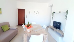 A living room with a sofa, a coffee table with a plant, a TV on a stand, and a wall clock. - CONCHIGLIA 3 minutes from the sea Relax and Holidays - on the Gulf of Castellammare.... (Alcamo)
