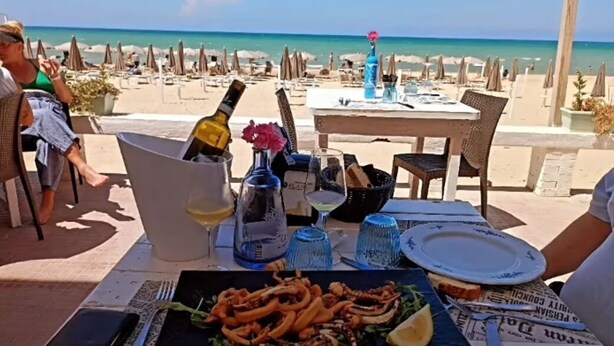 A table set for two with a seafood dish, wine glasses, and a bottle of wine. The table is outdoors with a view of the beach and ocean. - CONCHIGLIA 3 minutes from the sea Relax and Holidays - on the Gulf of Castellammare.... (Alcamo)