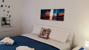 A hotel room with a bed, a nightstand, a dresser, a mirror, butterfly wall decor, and a sunset painting. - CONCHIGLIA 3 minutes from the sea Relax and Holidays - on the Gulf of Castellammare.... (Alcamo)
