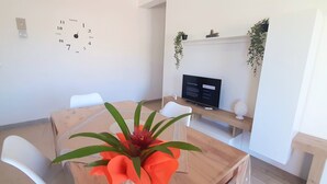 A modern room with a wooden table, white chairs, a clock on the wall, a television, and a shelf with plants. - CONCHIGLIA 3 minutes from the sea Relax and Holidays - on the Gulf of Castellammare.... (Alcamo)