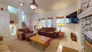 A spacious living room with a fireplace, leather sofas, a coffee table, and a stone wall. - On Golf Course | Pet Friendly | Nama-Stay (Angel Fire)