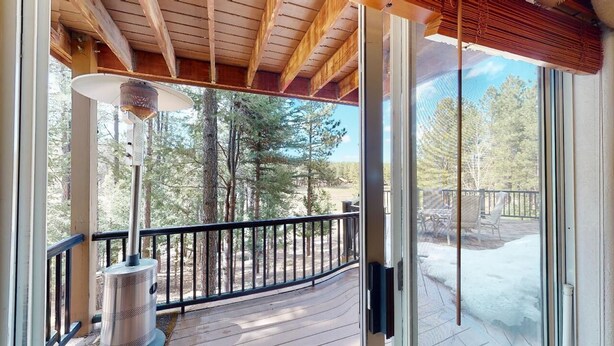 A wooden deck with a metal heater, a glass door leading to a snowy outdoor area, and a view of trees and a deck chair. - On Golf Course | Pet Friendly | Nama-Stay (Angel Fire)