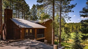 A rustic cabin with a metal roof, surrounded by tall pine trees, and a gravel driveway leading to a wooden deck. - On Golf Course | Pet Friendly | Nama-Stay (Angel Fire)