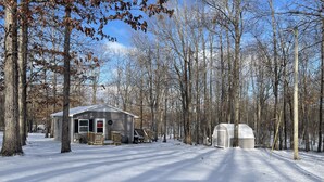 A cabin with a porch and a garage, surrounded by snow-covered ground and leafless trees. - Lake Cottage minutes away from downtown Sparta (Sparta)
