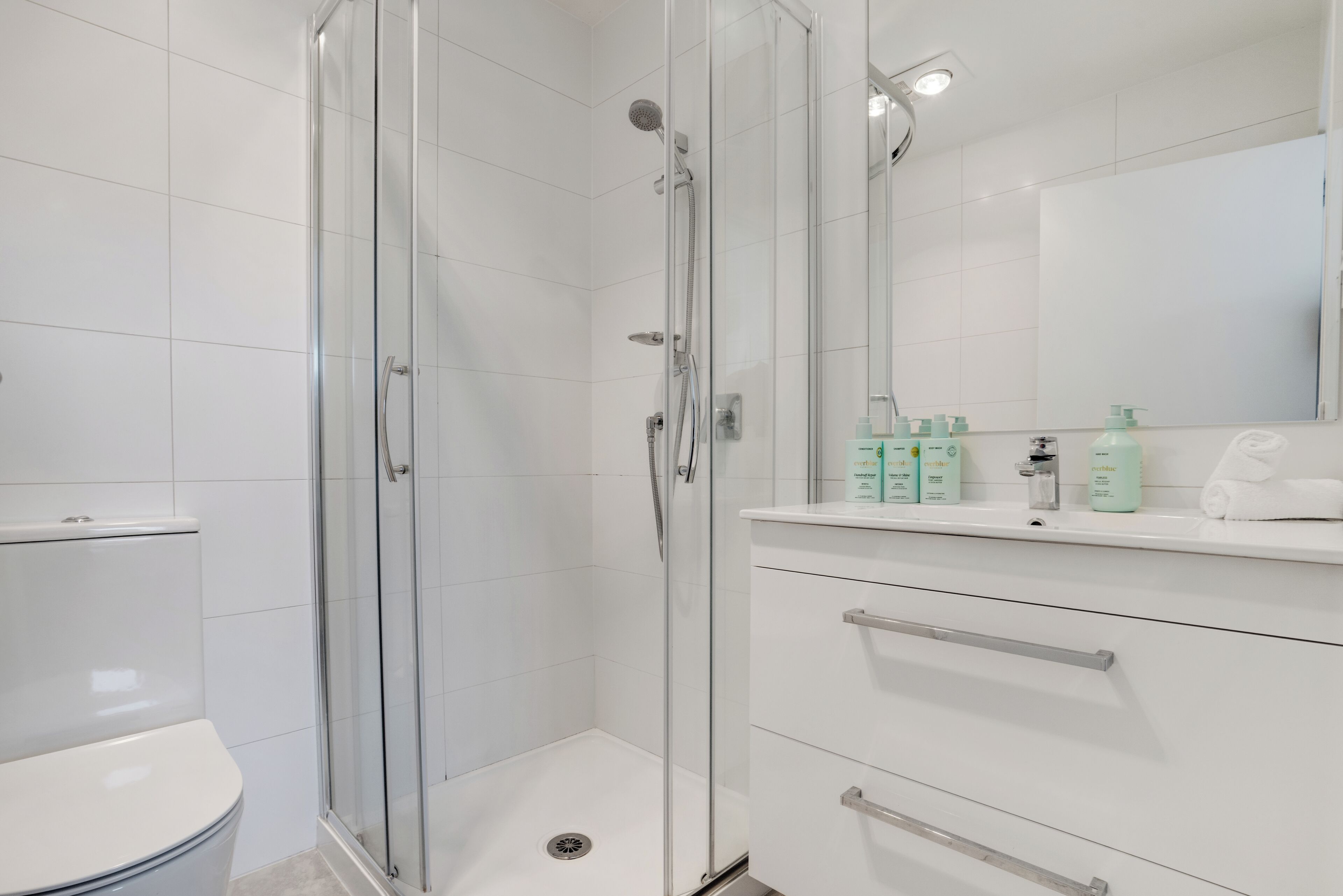 A modern bathroom with a glass-enclosed shower, a toilet, and a vanity with toiletries.