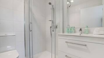 A modern bathroom with a glass-enclosed shower, a toilet, and a vanity with toiletries.