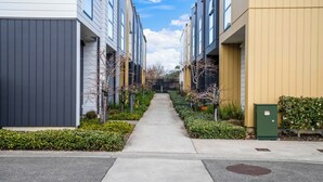 A modern apartment building with a central pathway, surrounded by greenery and featuring a mix of architectural styles. - Brand New House by Botany - Parking (Auckland)