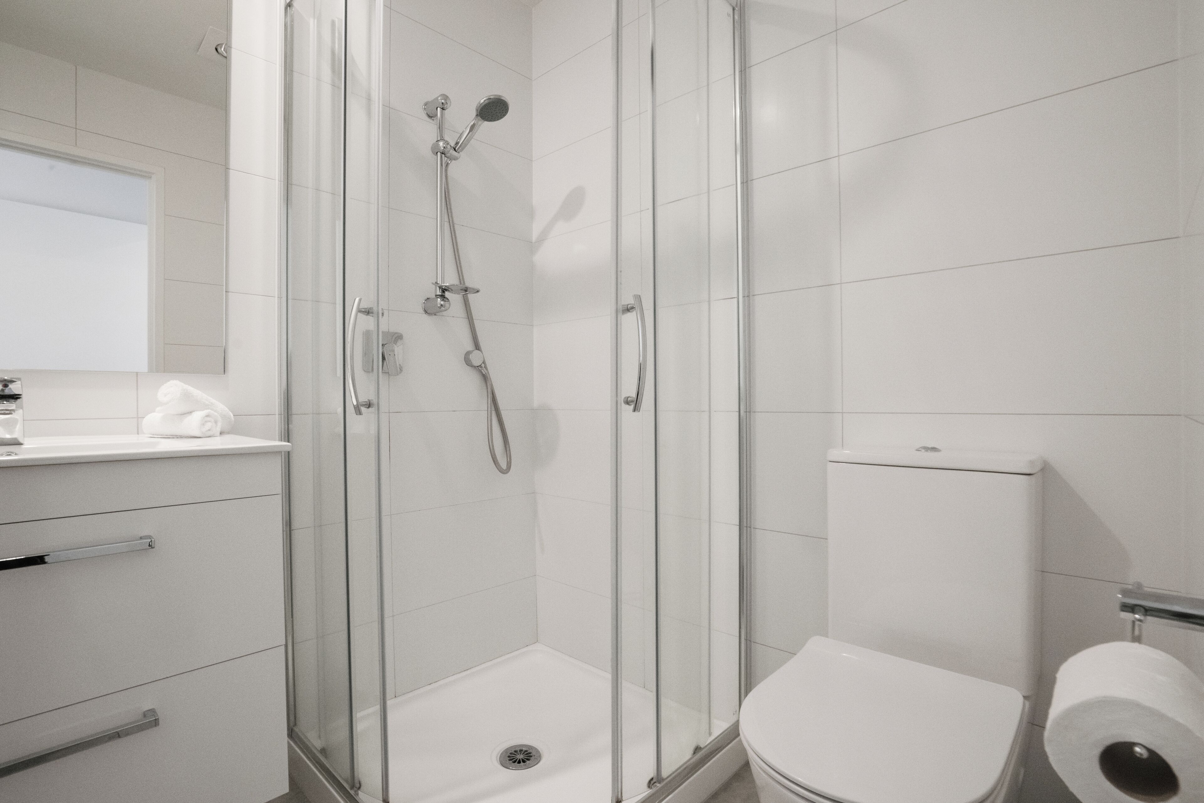 A modern bathroom with a glass-enclosed shower, a white toilet, and a sink with a towel.