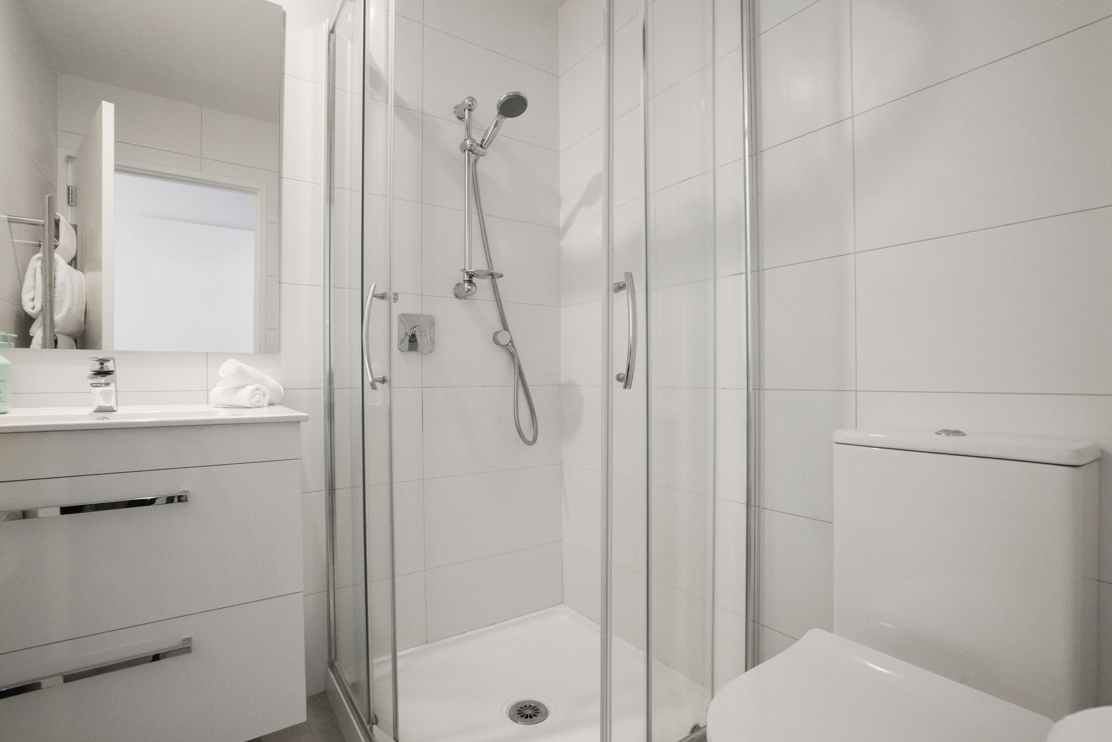Un baño moderno con ducha de vidrio, lavamanos blanco y retrete.