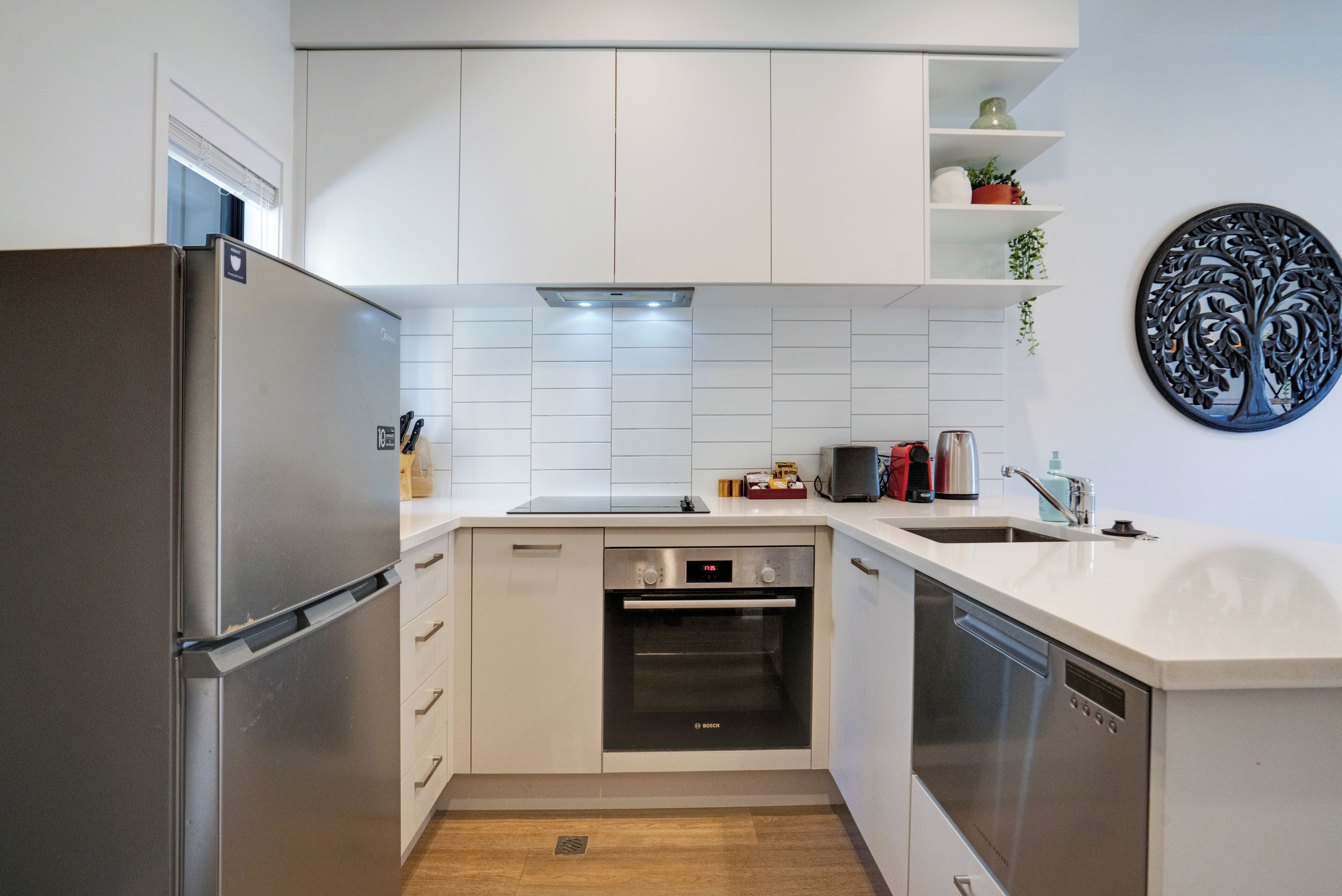 Una cocina moderna con armarios blancos, un refrigerador de acero inoxidable, un horno Bosch y un lavavajillas.