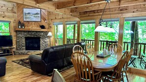 A cozy cabin interior with a stone fireplace, wooden walls, a leather sofa, and a dining area with wooden chairs. - Your Perfect Mountain Getaway Cabin in the Heart of Nature (Sevierville)