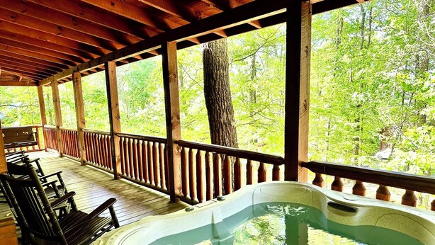A wooden deck with a hot tub and rocking chairs, surrounded by trees. - Your Perfect Mountain Getaway Cabin in the Heart of Nature (Sevierville)