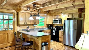 A wooden cabin-style kitchen with a central island, stainless steel appliances, and a view of the outdoors through large windows. - Your Perfect Mountain Getaway Cabin in the Heart of Nature (Sevierville)