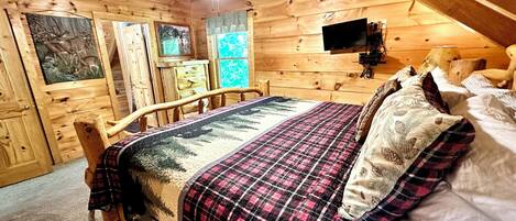 Un dormitorio de cabaña de madera con una cama, un ventilador de techo y un televisor.