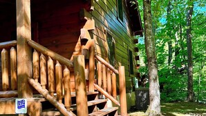 A rustic cabin with a wooden staircase leading to a porch, surrounded by trees. - Your Perfect Mountain Getaway Cabin in the Heart of Nature (Sevierville)