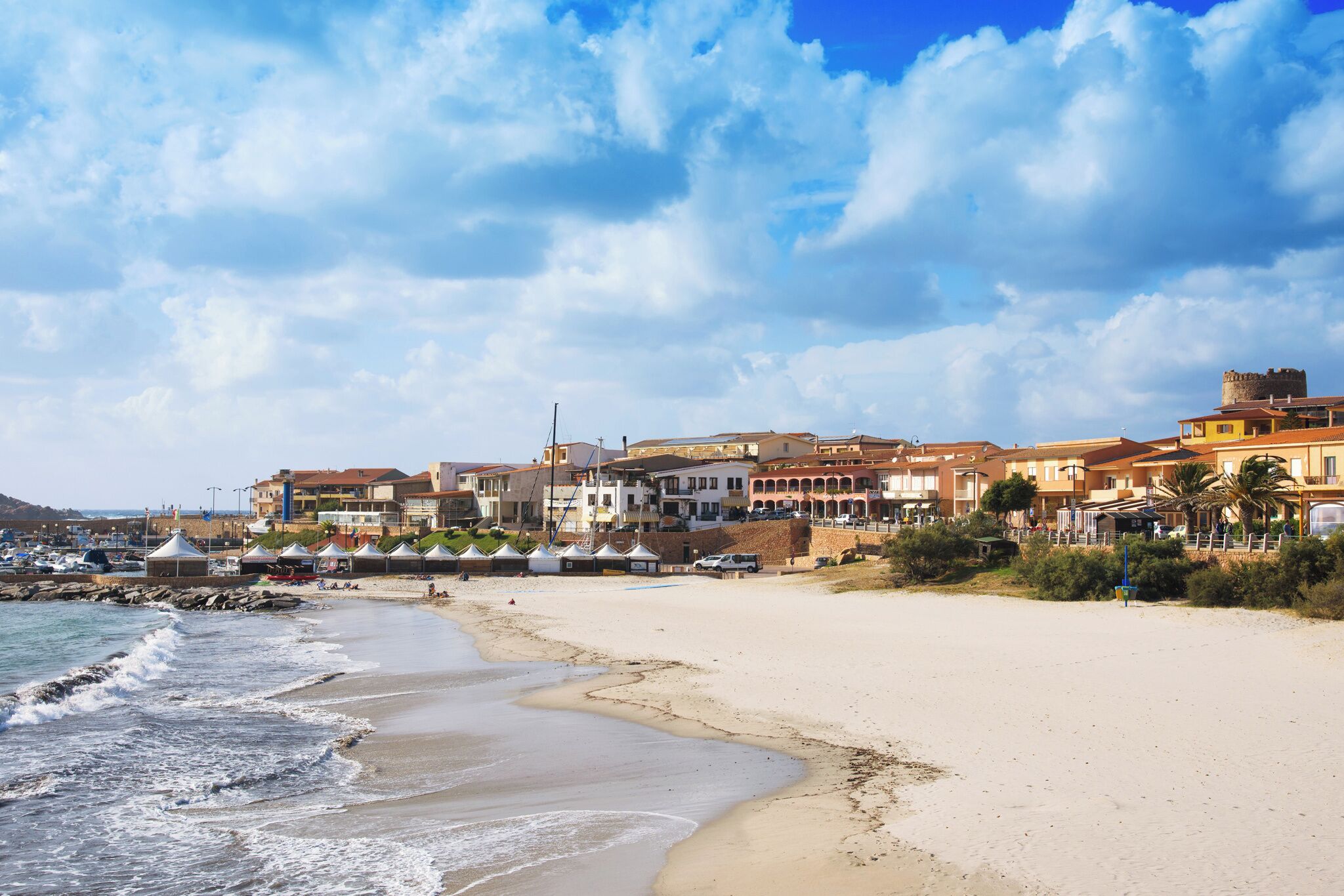 Eine Küstenstadt mit Sandstrand, Häusern mit Balkonen und einer Turmstruktur.