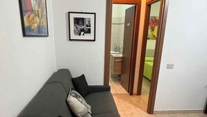 A living room with a dark-colored sofa, two pillows, a framed black-and-white photo, and a colorful painting on the wall. - Holiday apartment for exclusive use with auxiliary heating (Lurago D'erba)