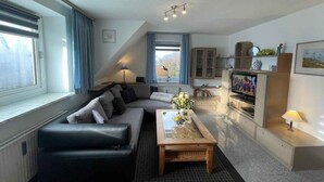 Een moderne woonkamer met een zwarte leren bank, een houten salontafel en een televisie.