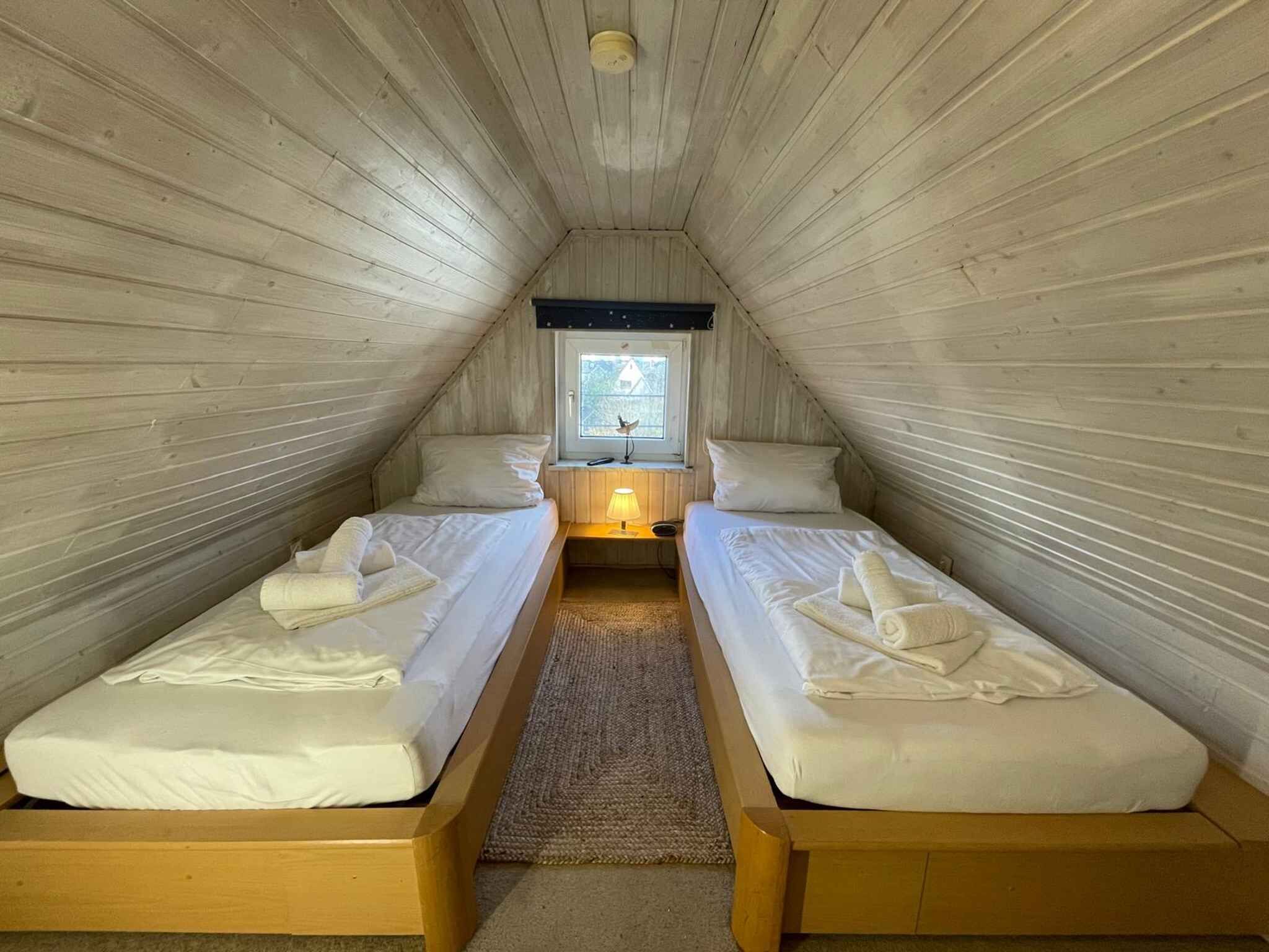 A small, cozy attic bedroom with two single beds, a window with a view, and a ceiling light.