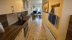 Una cocina moderna con una isla central, una zona de comedor con mesa y sillas, y un espacio de estar con televisor y asientos.