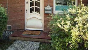 Una casa con puerta blanca, una ventana pequeña y fachada de ladrillo.