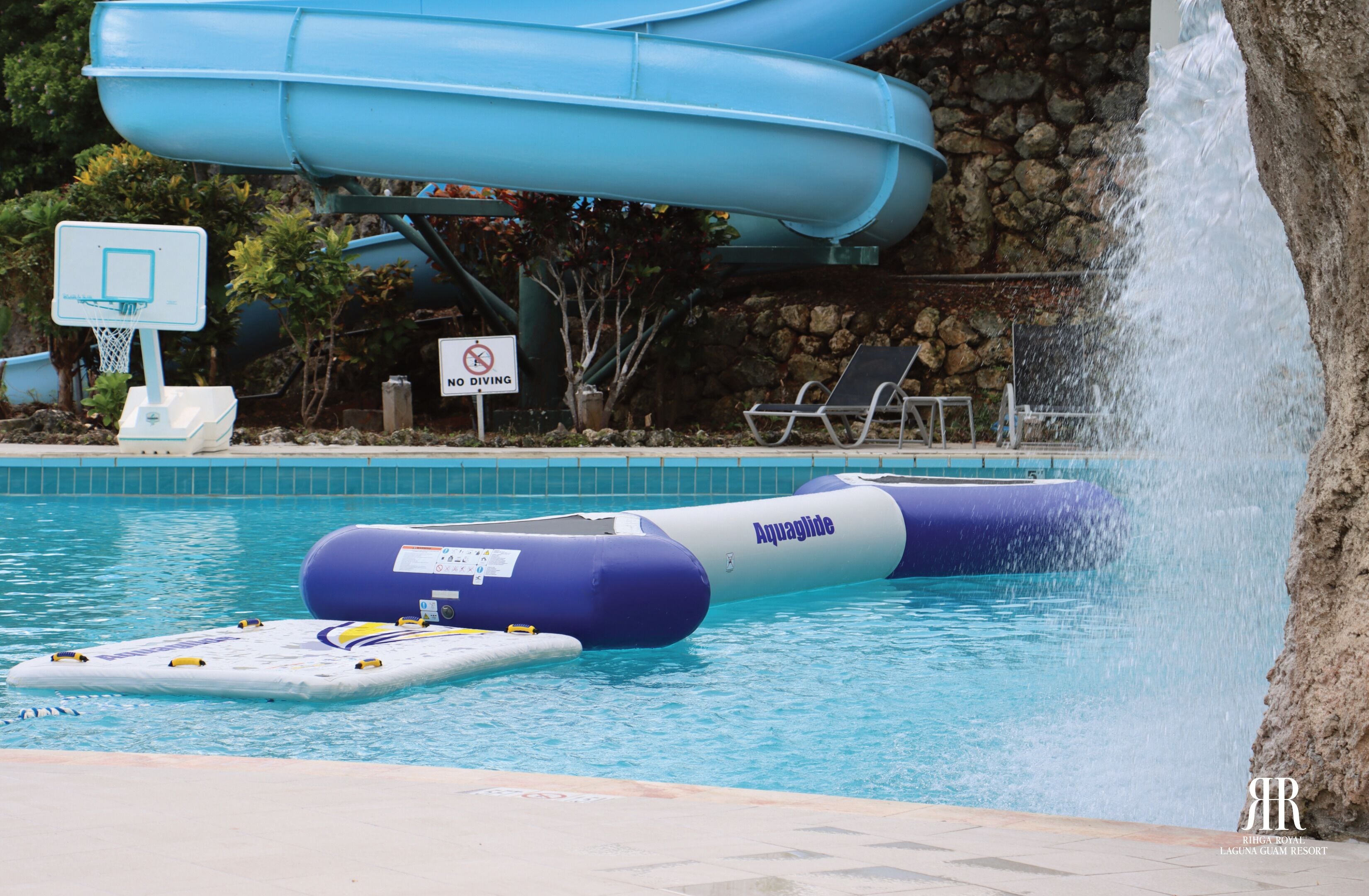 Una piscina con toboganes, un cartel de prohibido bucear y sillas de descanso.