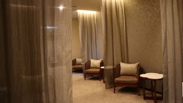 A hotel room with a carpeted floor, two wooden chairs, a small table, and a large window with curtains.