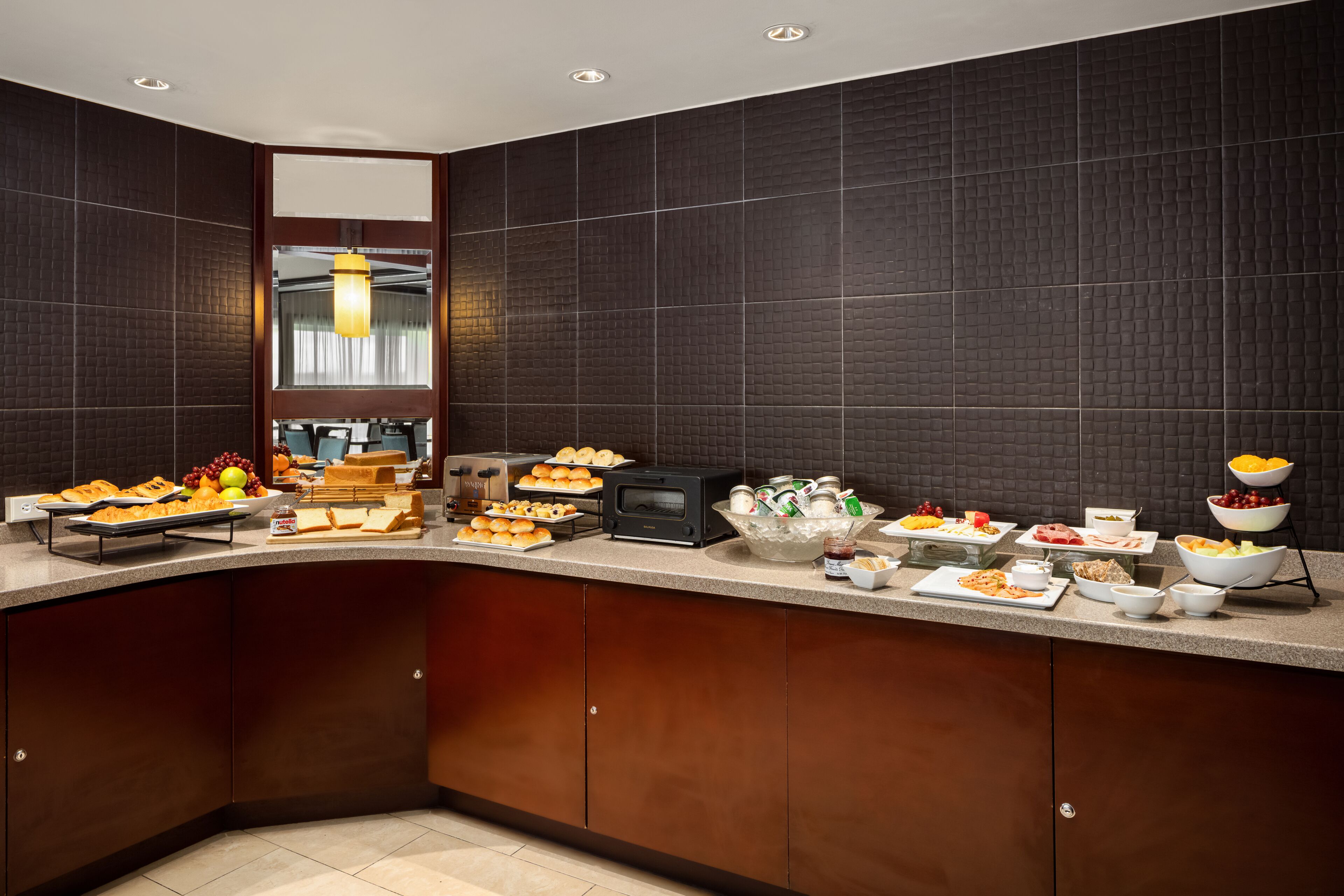 A modern kitchen with dark tiled walls, a wooden cabinet, and a variety of breakfast items on the counter.
