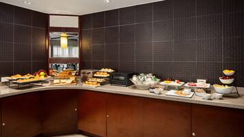 A modern kitchen with dark tiled walls, a wooden cabinet, and a variety of breakfast items on the counter.