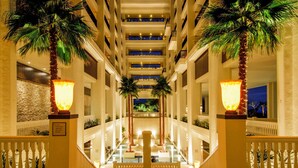 A multi-level hotel atrium with a central pool, palm trees, and illuminated fixtures.