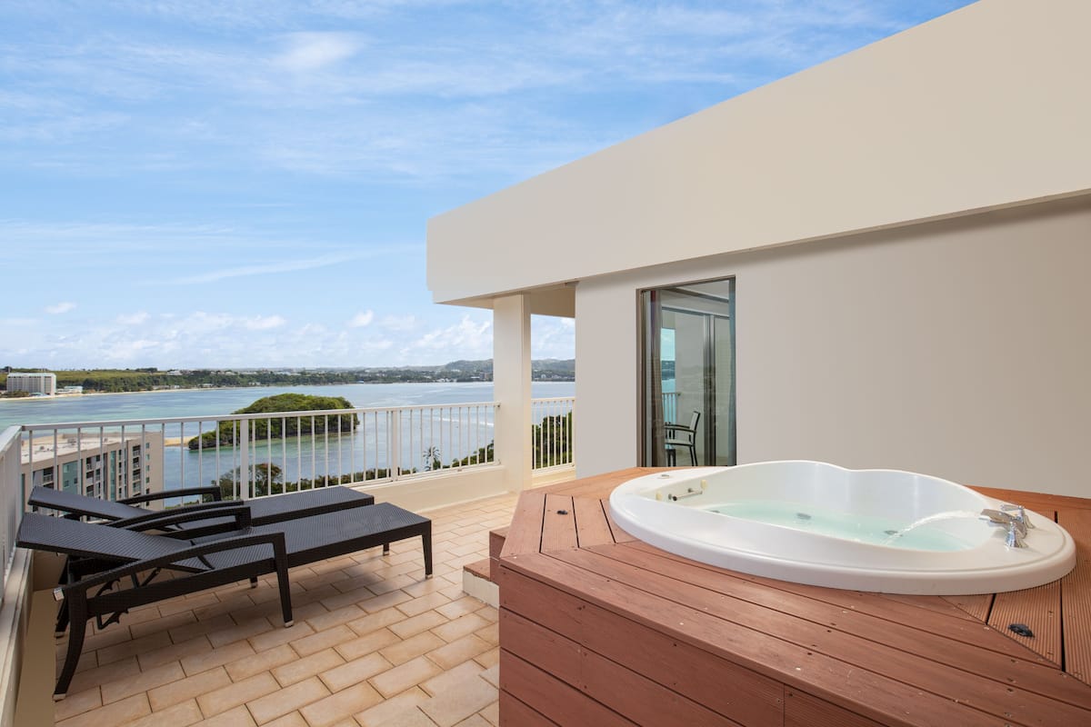 A balcony with a hot tub, lounge chairs, and a view of the sea.