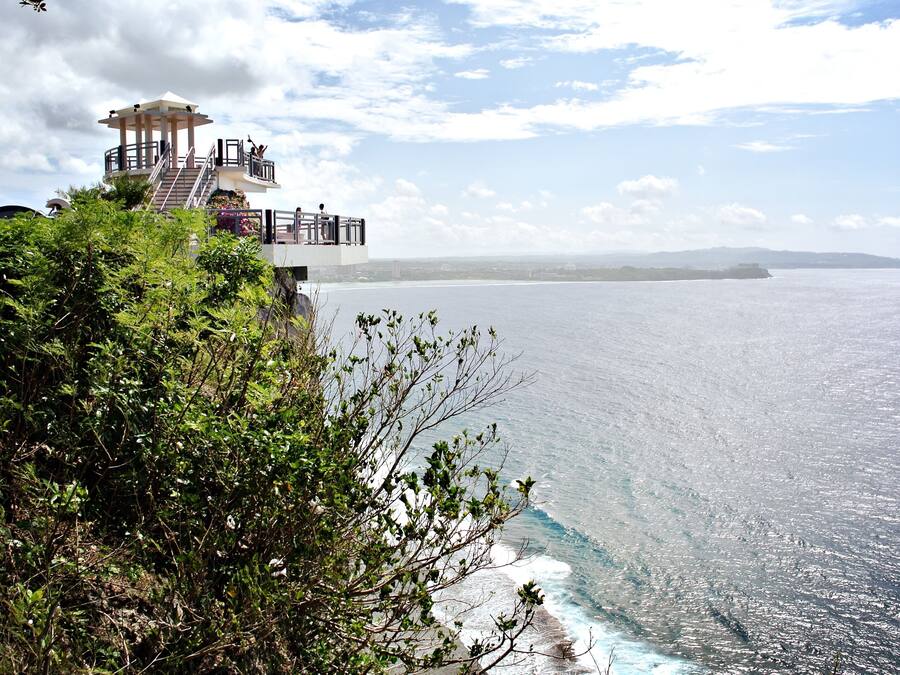 Vista costera con una estructura similar a un pabellón en un acantilado con vista al mar.