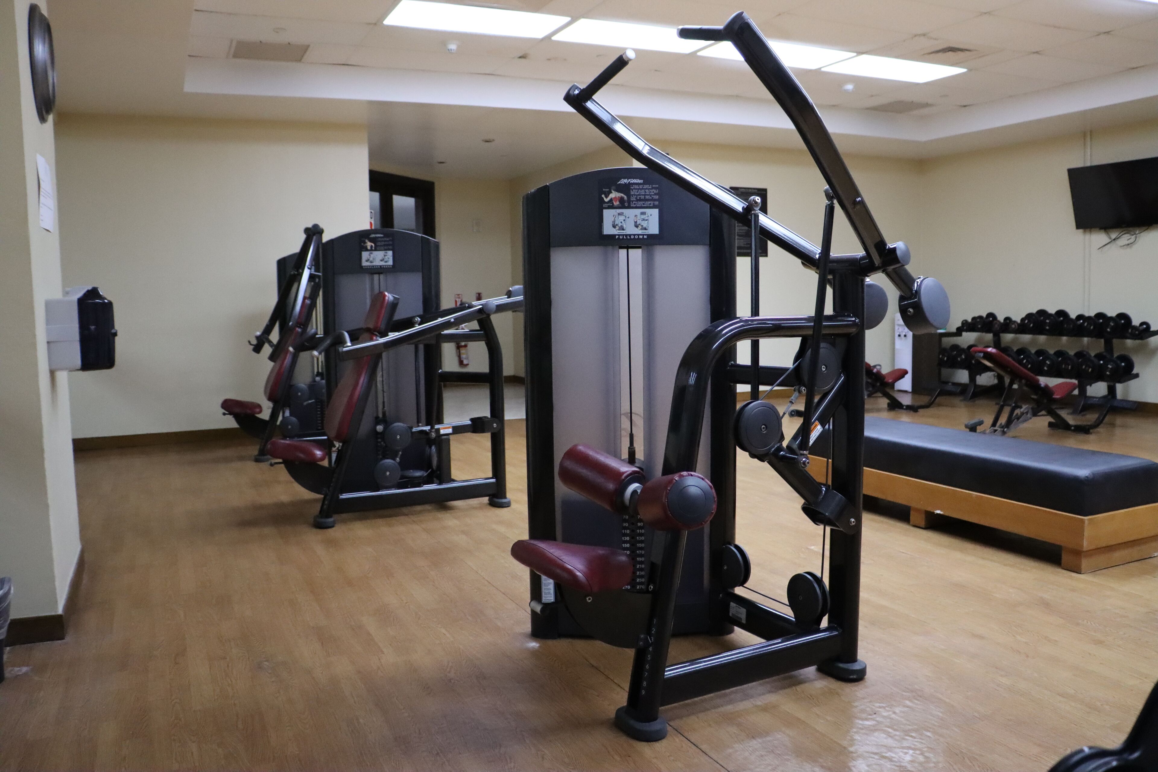 Un gimnasio con equipo de ejercicio, una banca y un televisor instalado en la pared.